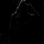 A silhouette of a person against a dark background with light filtering through foliage above.