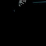 A shadowy and atmospheric portrait of a person partially illuminated, with deep contrasts obscuring much of the detail, creating a moody and enigmatic scene.