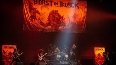 A dynamic metal band performing onstage, with intense lighting and a backdrop featuring fierce beast-themed artwork.