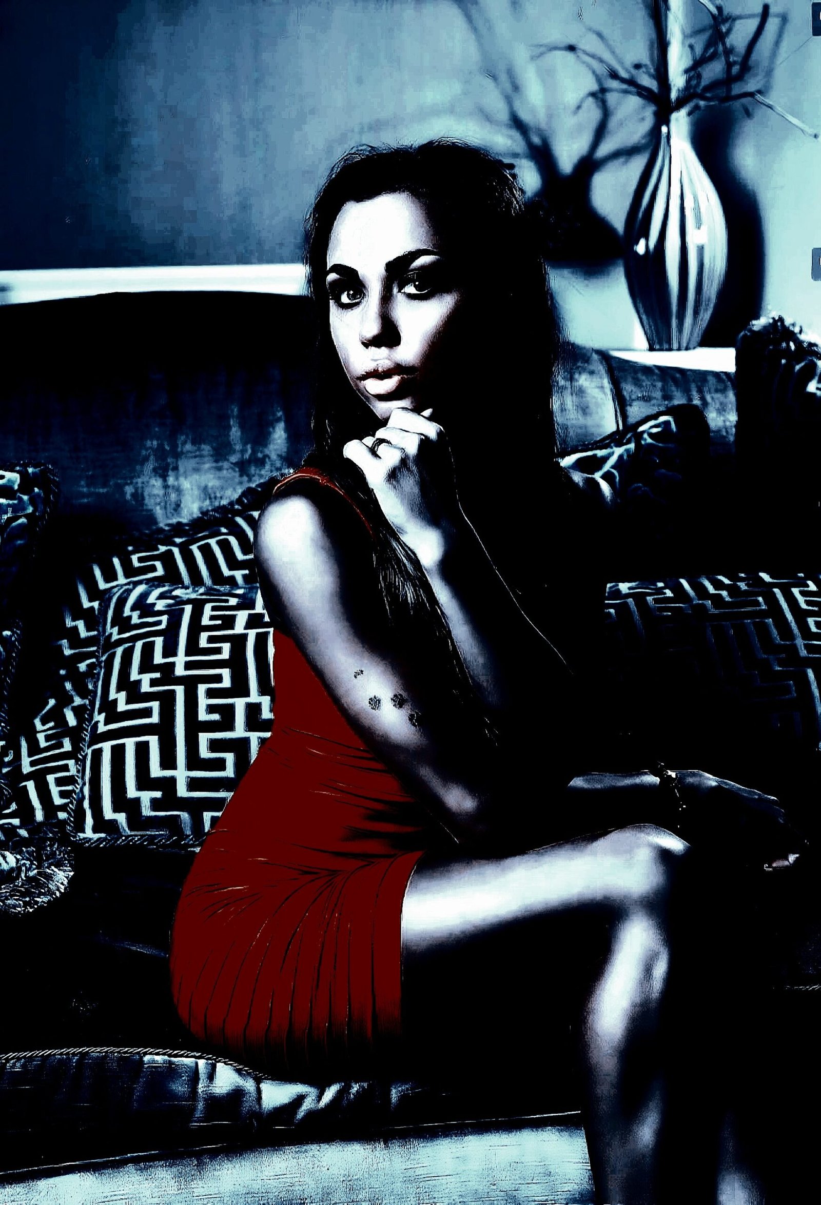 Woman in a red dress sitting on a sofa, posing thoughtfully with a calm, serious expression in a sophisticated living room setting.