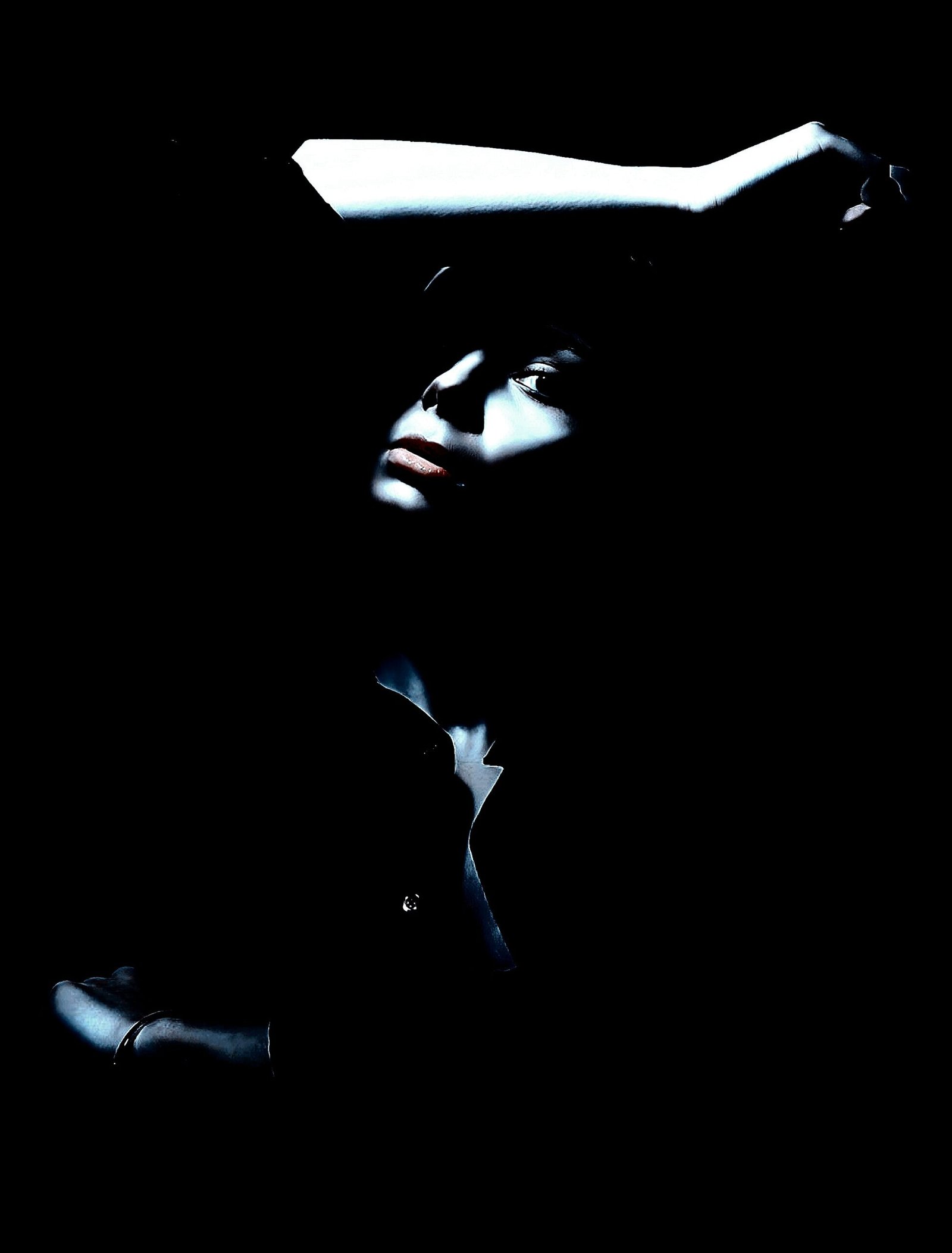 Woman partially illuminated with an arm raised, showcasing her face in shadows with a moody, introspective expression.