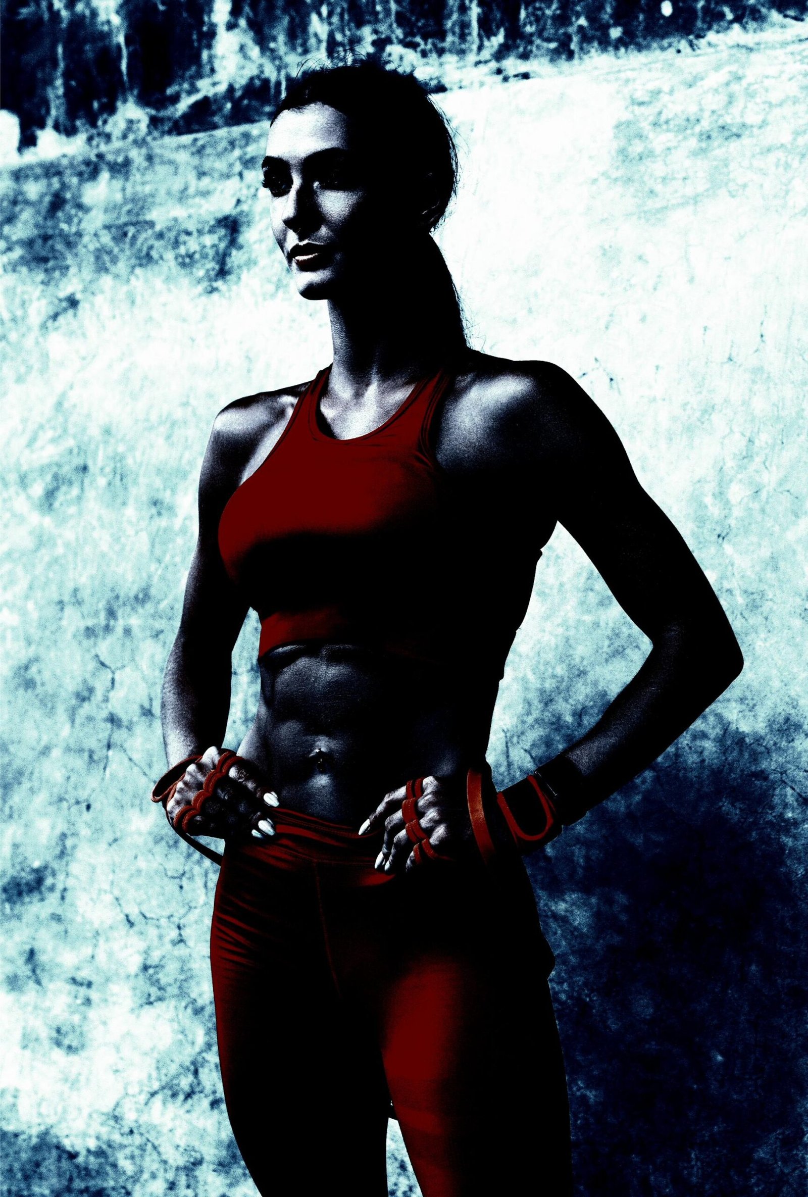 A woman standing confidently in a red sports bra and leggings, her defined abs and toned arms visible, exuding strength and determination.