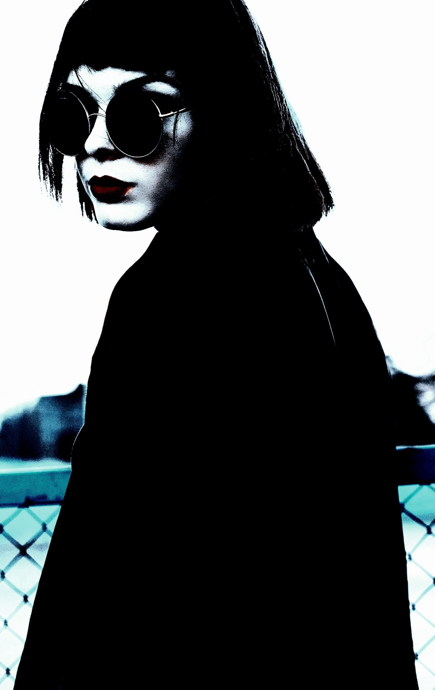 Close-up of a person in dark sunglasses and black attire, with a bold red lip, embodying a classic rock vibe.