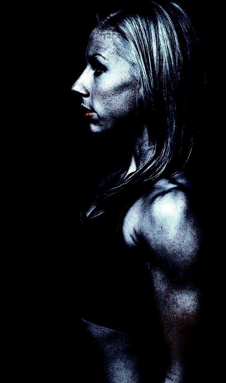 Profile of a strong woman with defined features and toned muscles, illuminated in dramatic, shadowy lighting.
