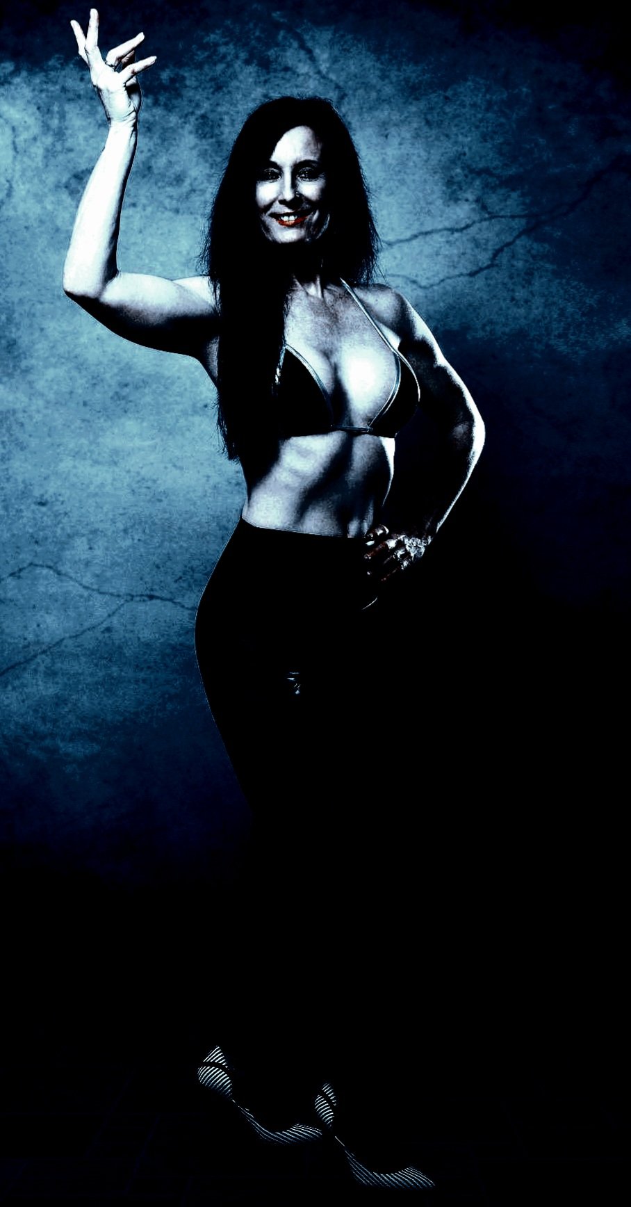 A confident woman in a bikini striking a powerful pose with a bold smile against a textured, dark background.