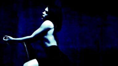 Artistic goth fashion scene with a woman in a black outfit posing expressively against a textured blue background.
