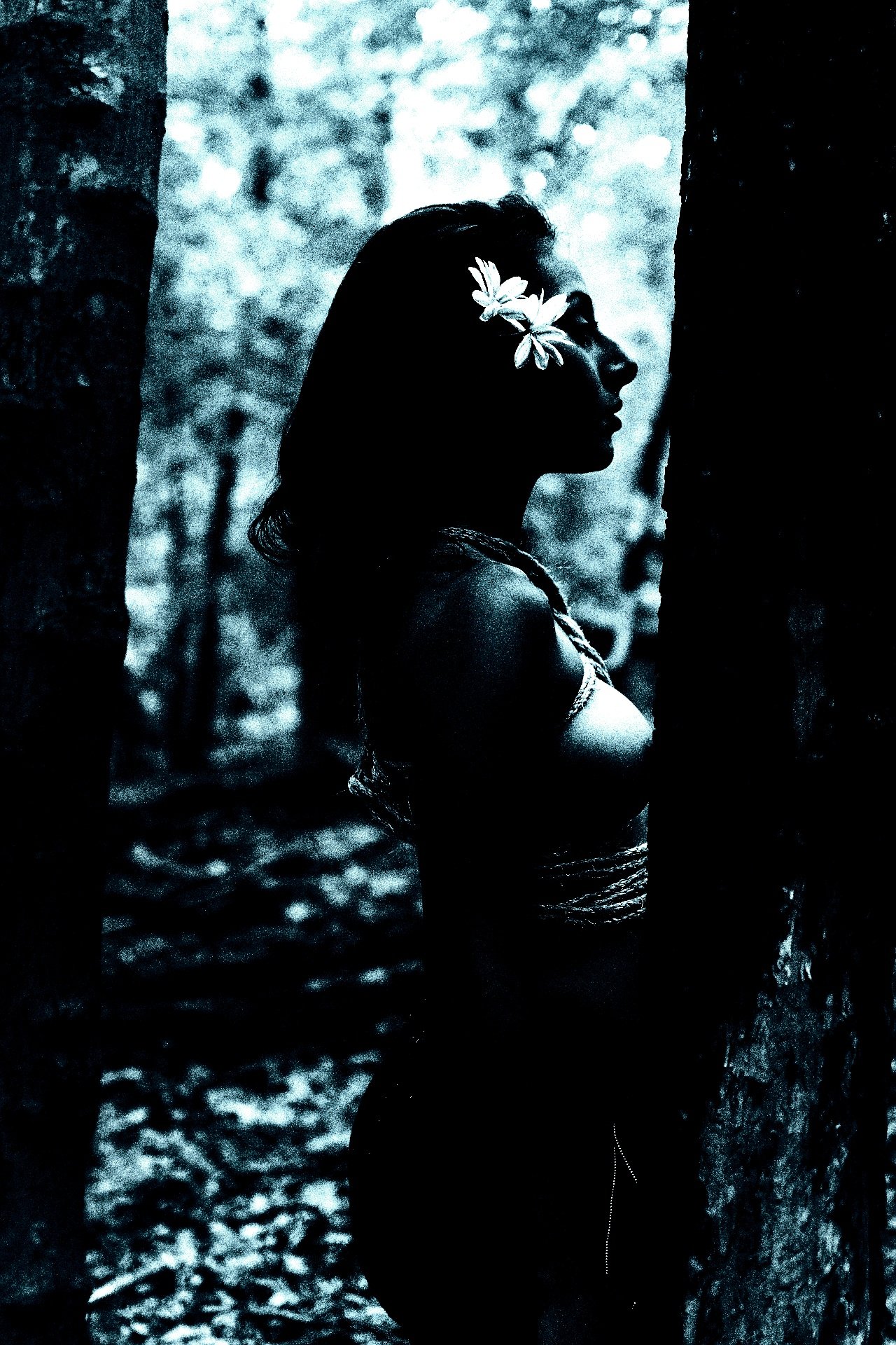 A gothic woman stands with eyes closed in a serene pose, dressed in a simple black skirt against a dark blue background.