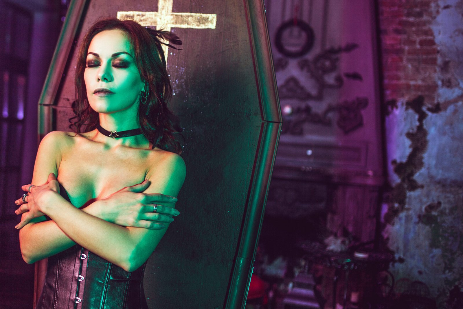 A woman in a gothic ensemble standing against a coffin, conveying a somber elegance in a room of antique decor.
