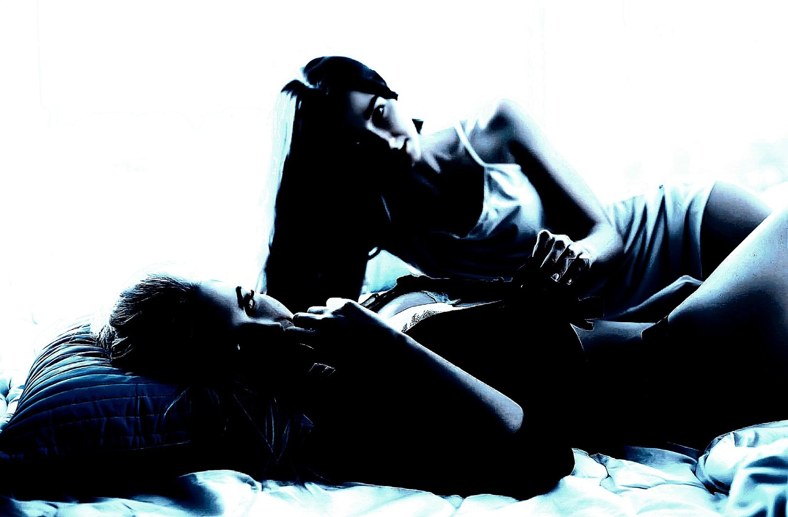 Two women with a lesbian undertone in a contemplative gothic pose on a bed.