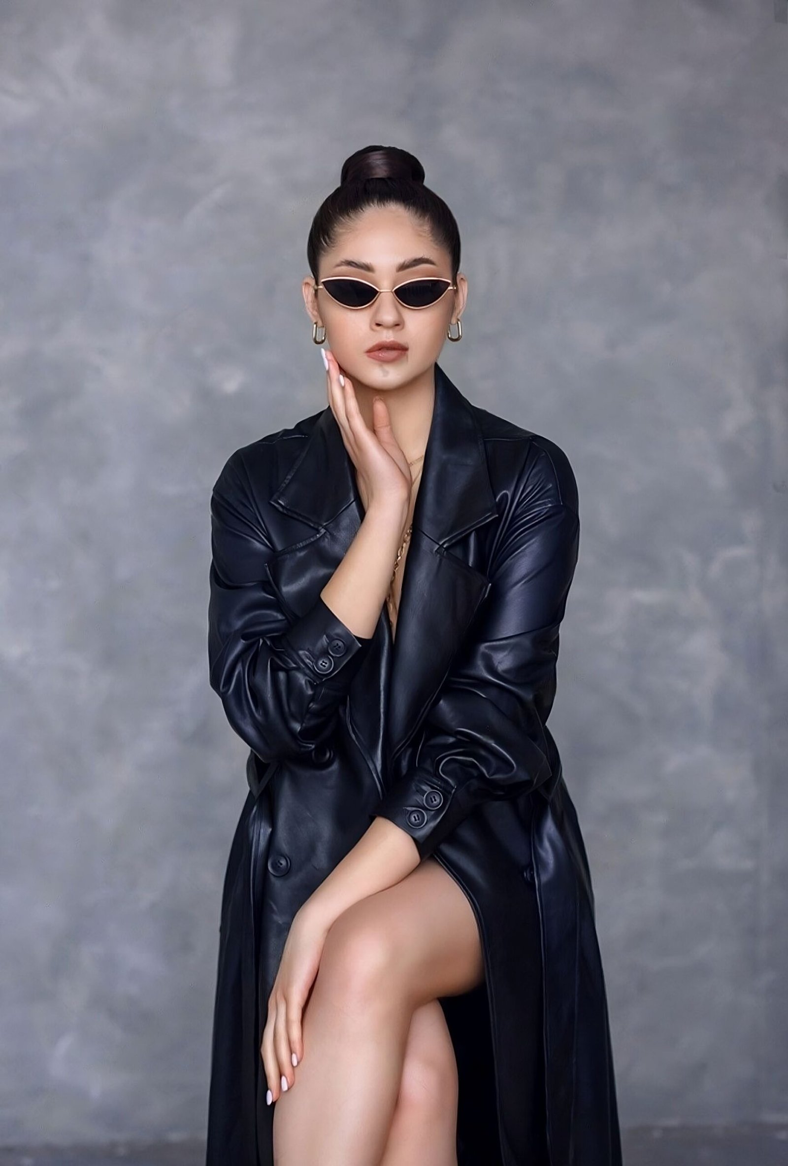 Stylish woman in sunglasses and a black leather trench coat, with a poised and contemplative expression.