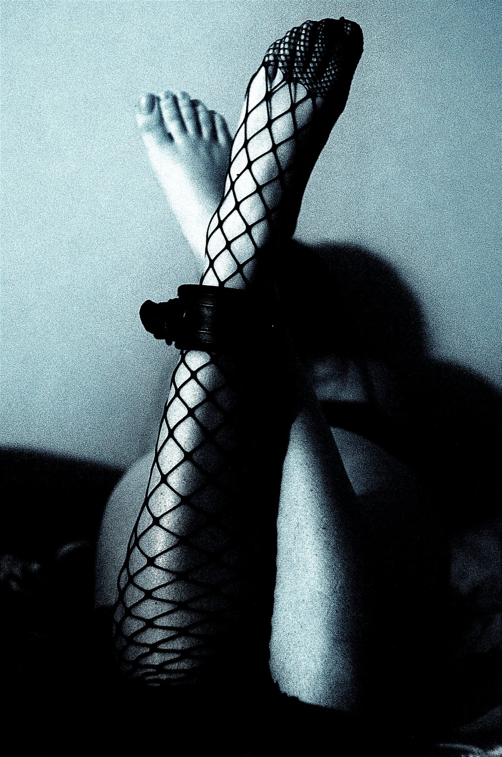 Silhouetted figure wearing fishnet stockings, the pattern creating dramatic shadows across the legs, encapsulating a sense of allure and mystery.