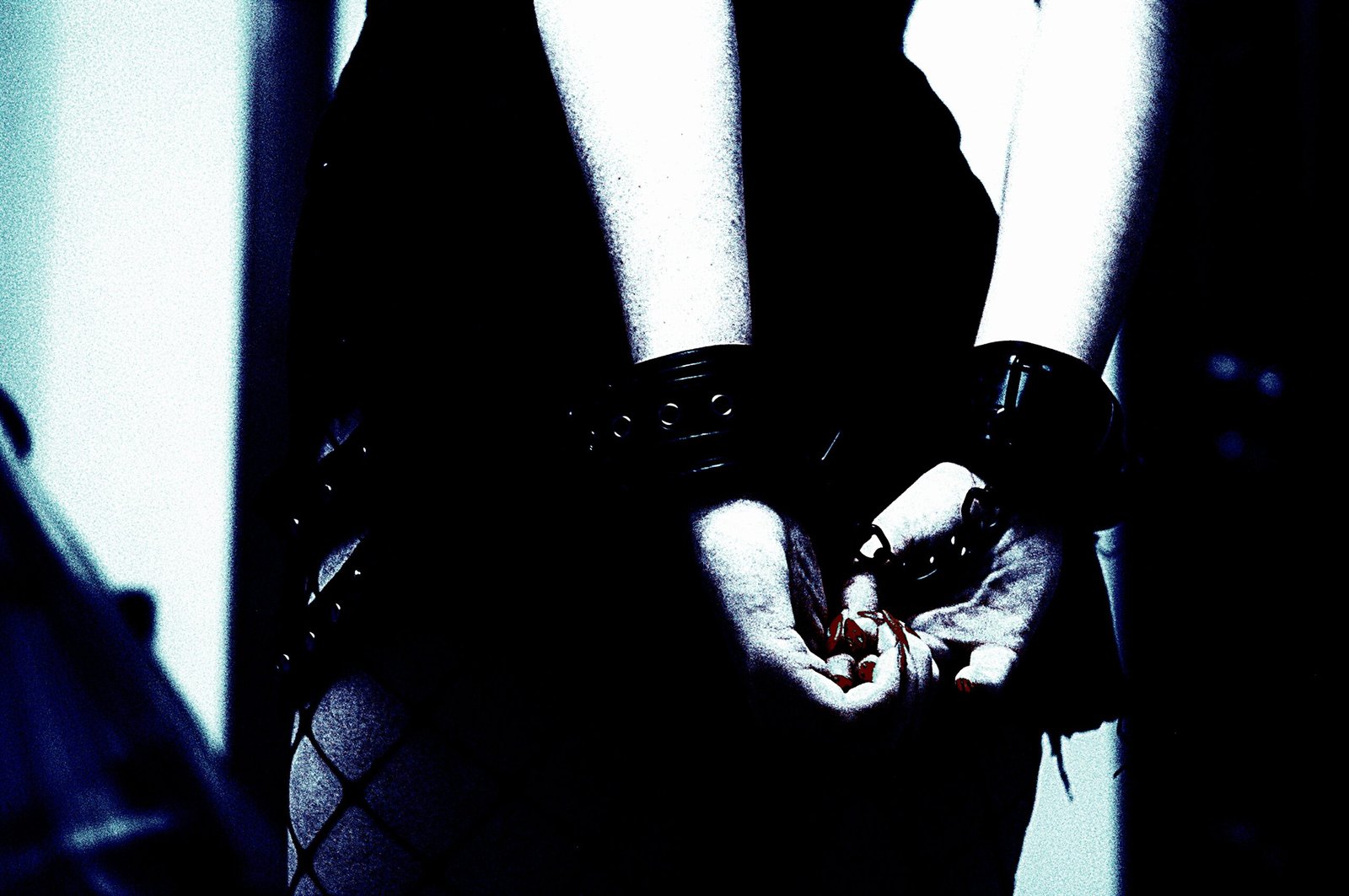 Trust and Consent in Bondage Play: A close-up black and white photo of a person's hands gently clasped together, with the wrists secured by leather cuffs, conveying vulnerability and trust.