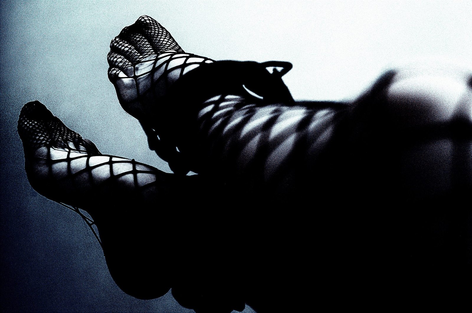 Intense monochrome photo focusing on a person's clasped hands with bondage cuffs, set against a dark background, highlighting themes of control and consent in BDSM play.