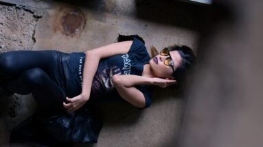 Woman in a relaxed pose exuding Victorian grandeur meets modern edge with Iron Maiden tee and leather leggings.