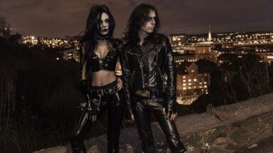 Gothic duo overlooking Gothenburg's nightscape, embodying the spirit of Blind Guardian