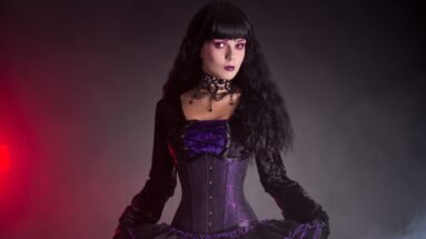 Woman modeling a velvet gothic corset dress with intricate lace details and purple accents.