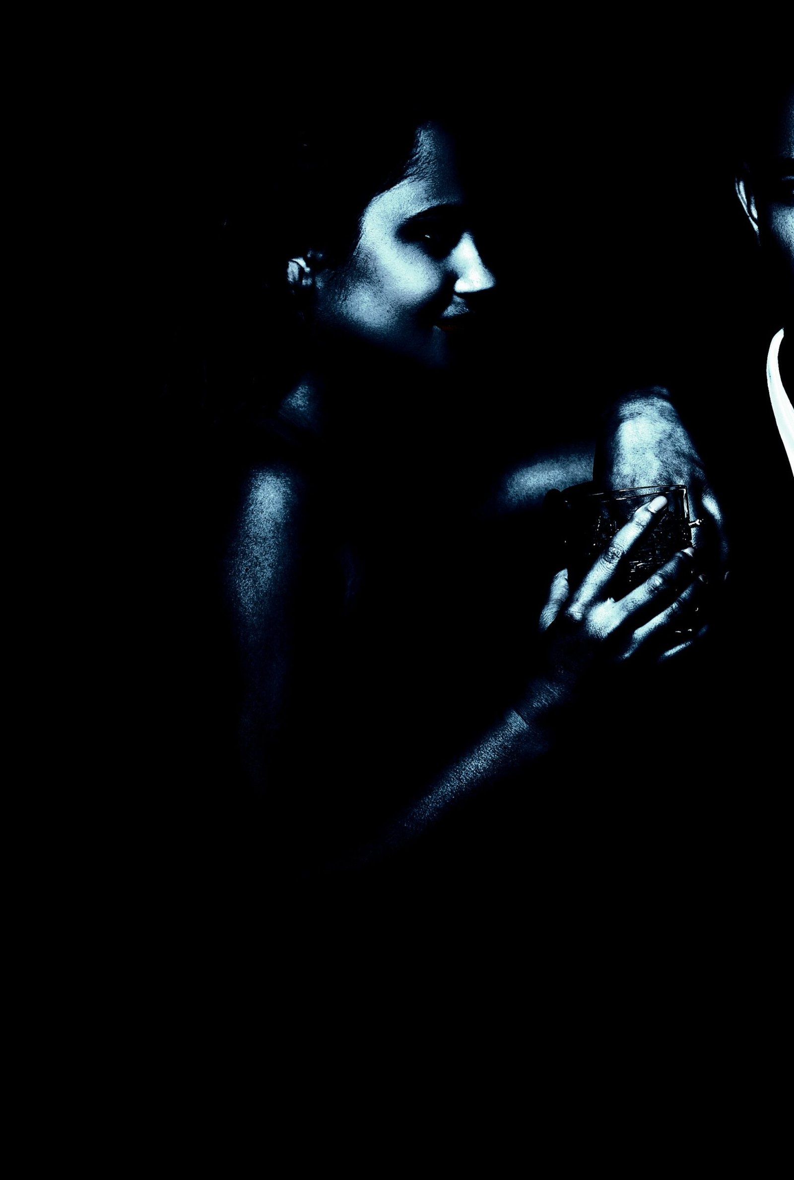 A close-up of a smiling woman being embraced by a man, both bathed in a moody blue light.