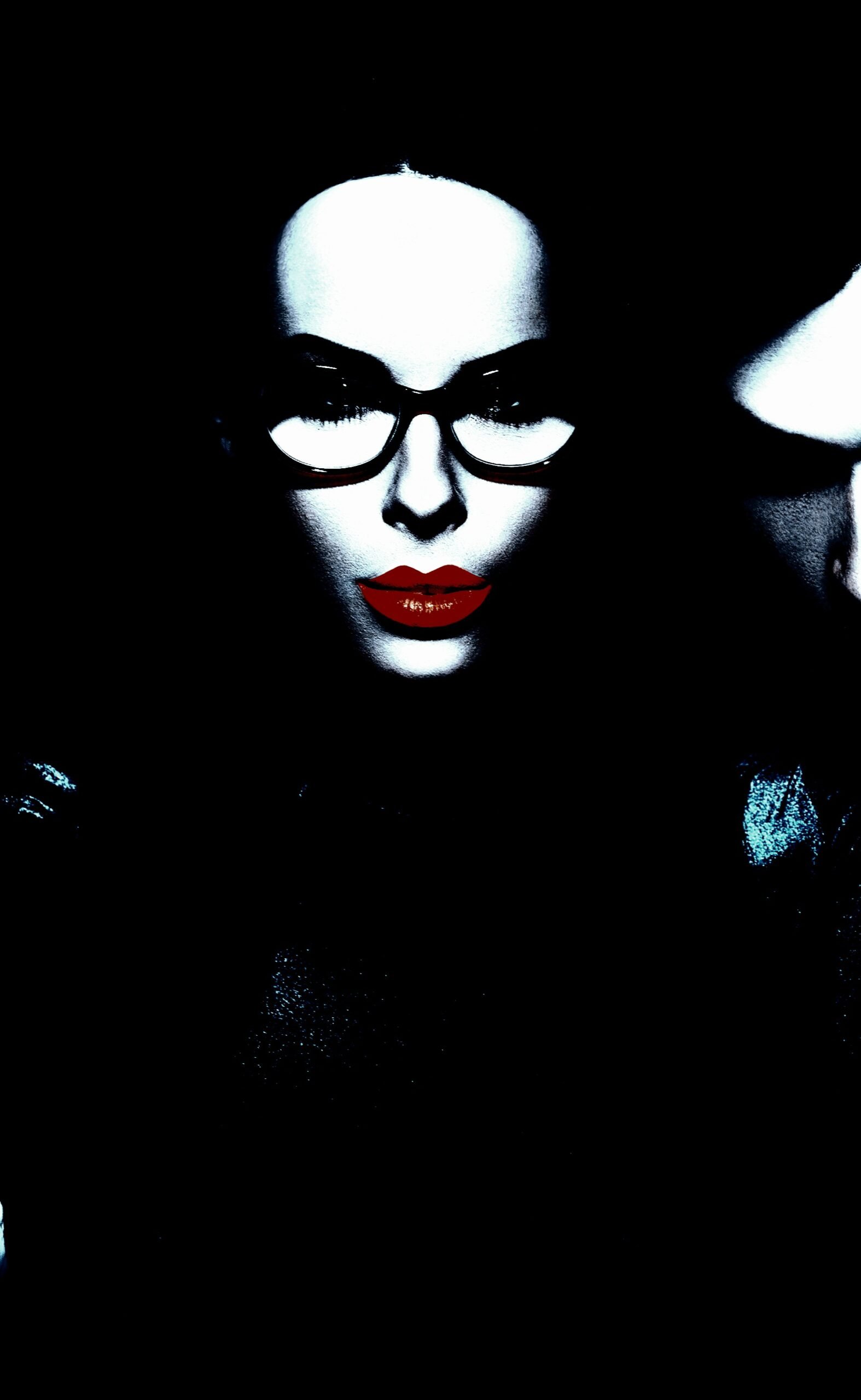 A striking image of a woman wearing glasses, with pronounced red lips, set against a pitch-black background.