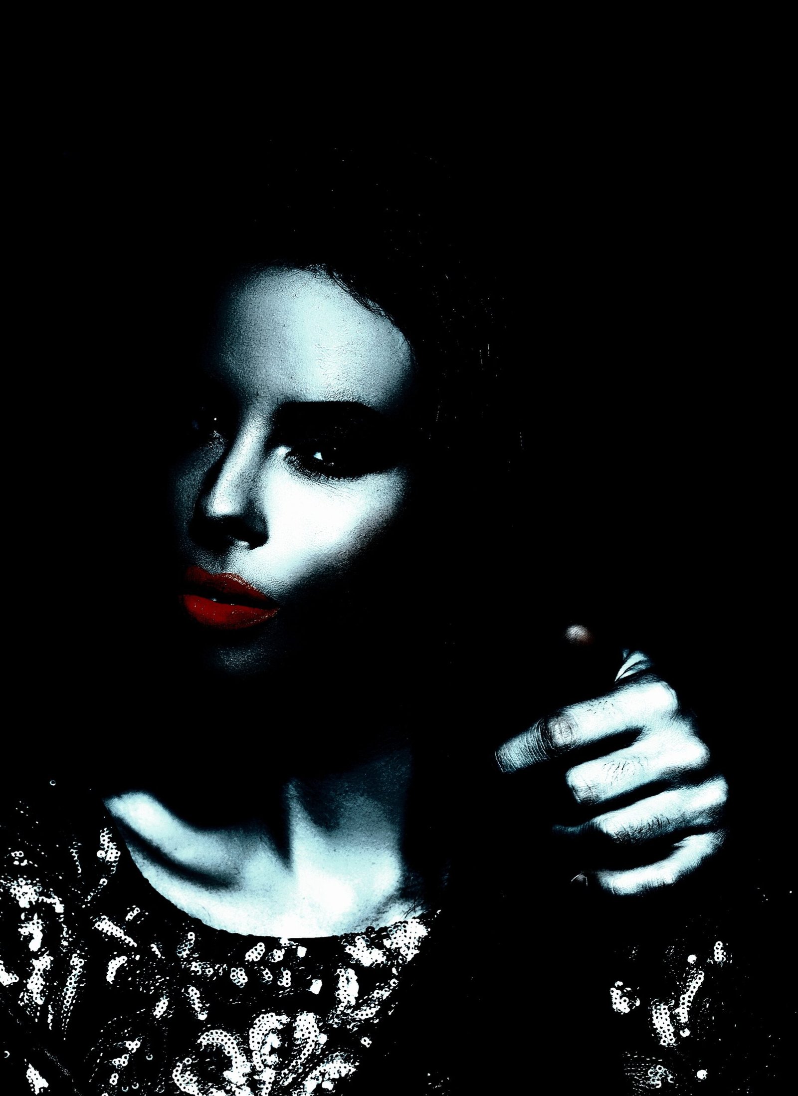 A woman with an intense gaze, featuring highlighted red lips and a sequin dress, shrouded in shadows.