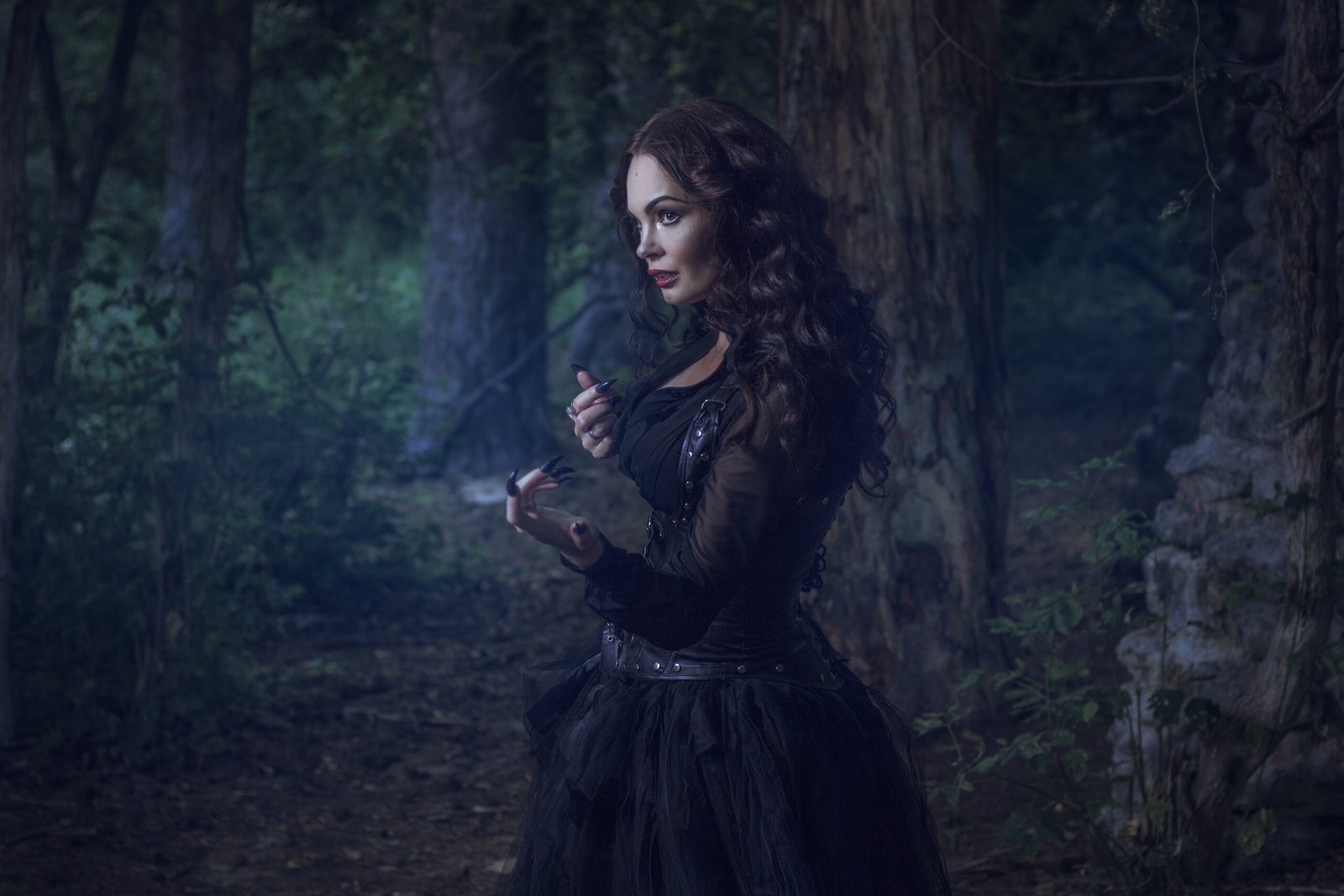 Gothic woman with dark makeup in a forest, exuding Victorian allure with a corseted dress.