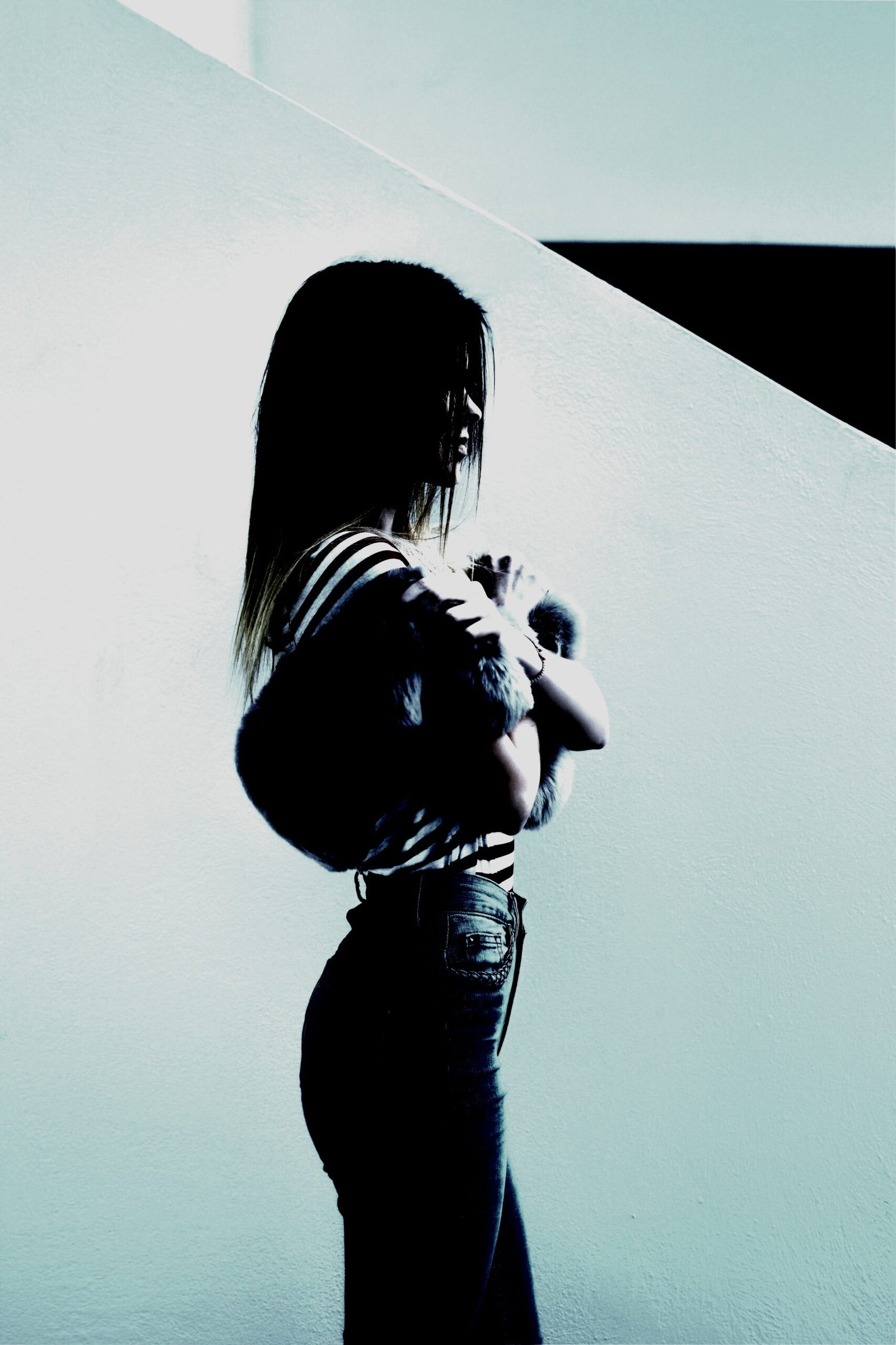 A woman in a striped top and jeans, standing in a starkly lit corner with a moody atmosphere.