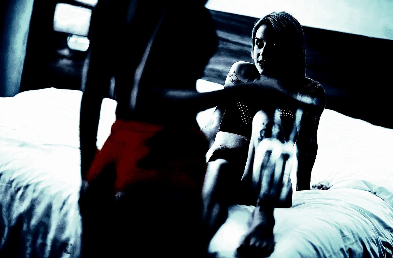 A dramatic and intimate scene with two women on a bed, one seated and the other lying down, engaging closely.