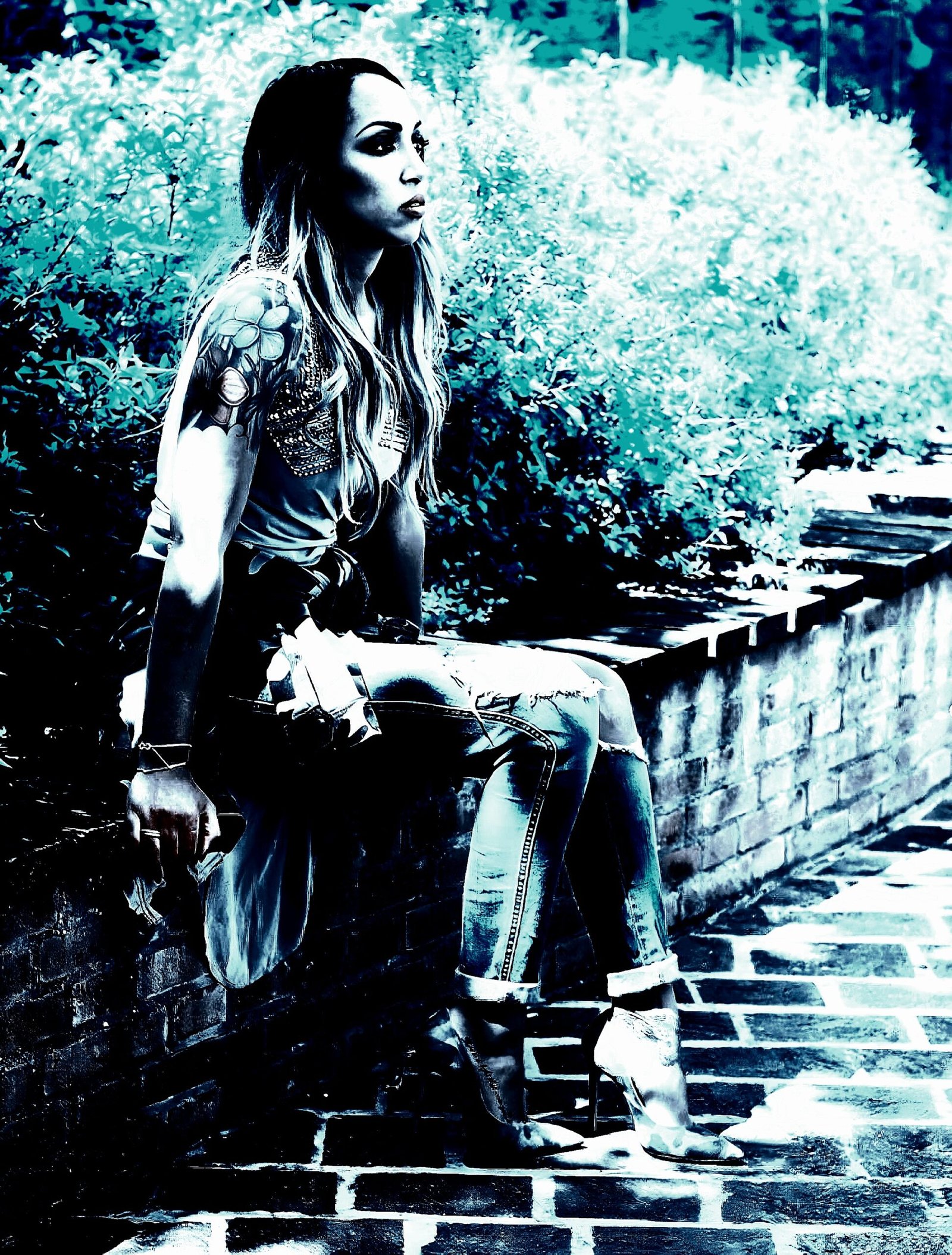 Woman sitting on a stone bench outdoors, wearing a casual outfit and high heels, looking off into the distance with a pensive expression.