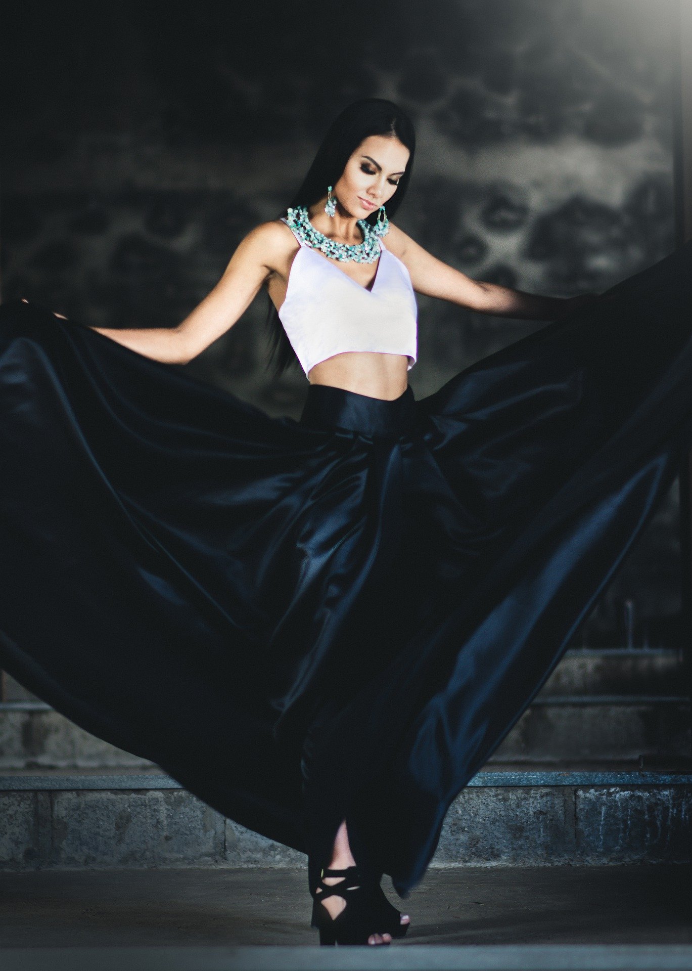 Woman in a stylish Hot Vampire Halloween Costume, featuring a flowing black skirt and white crop top with elaborate jewelry.