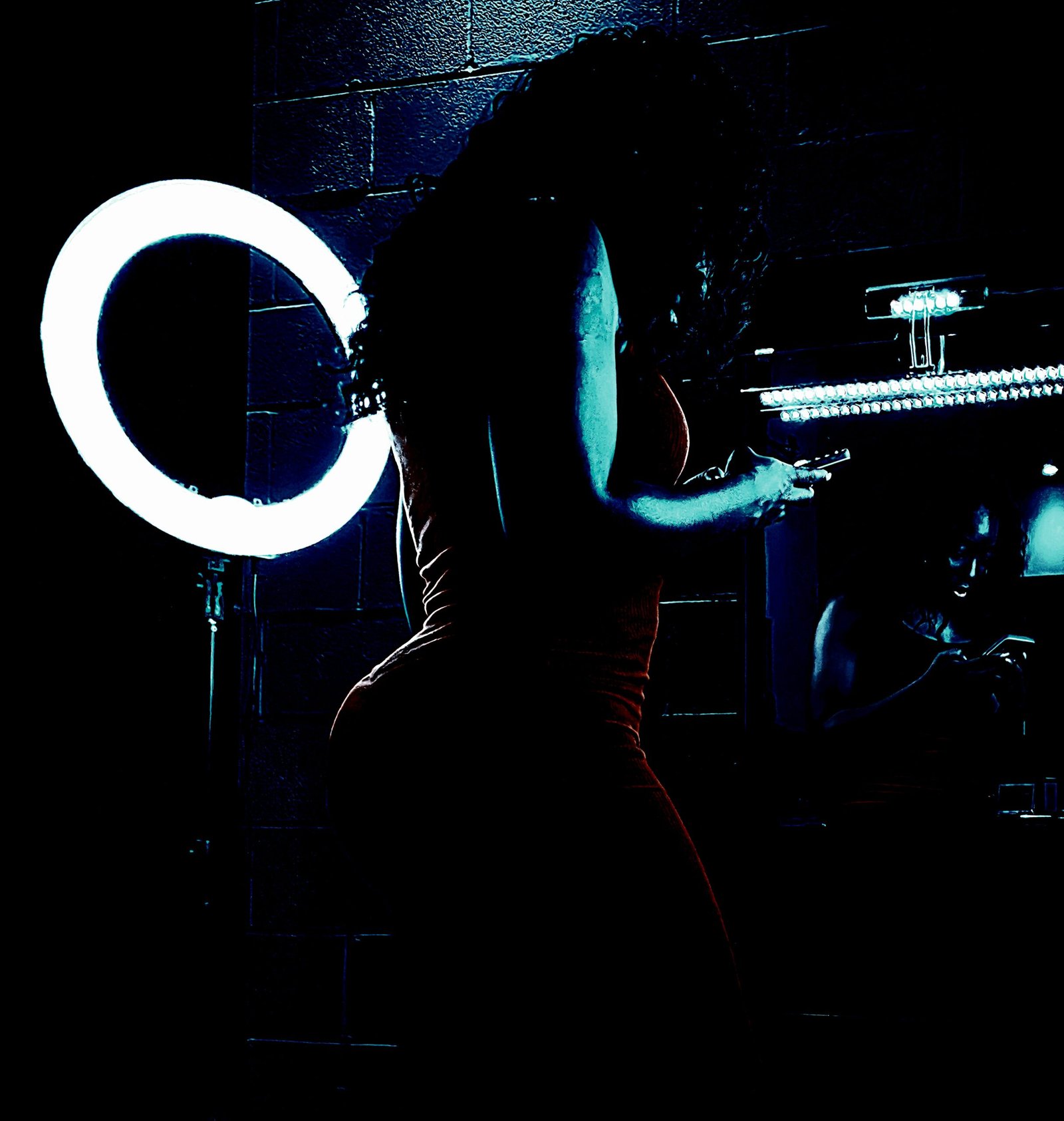 Silhouette of a woman in a tight dress using her phone, illuminated by a ring light, in front of a mirror.