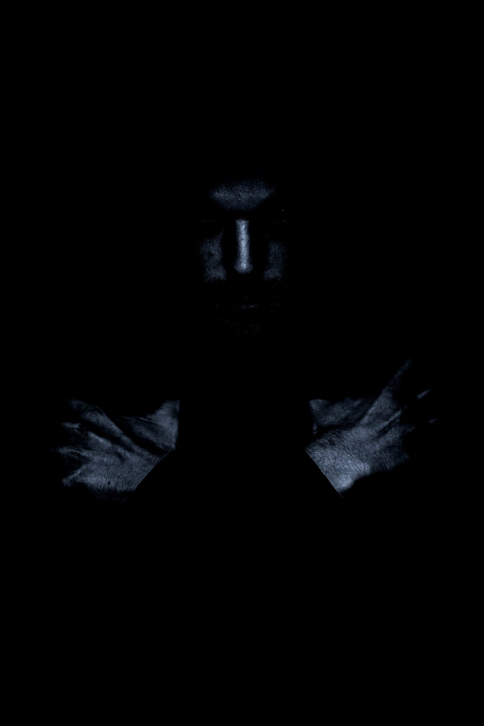 Mysterious male figure in dark clothes, visible only as a silhouette with glowing eyes in a completely dark setting.