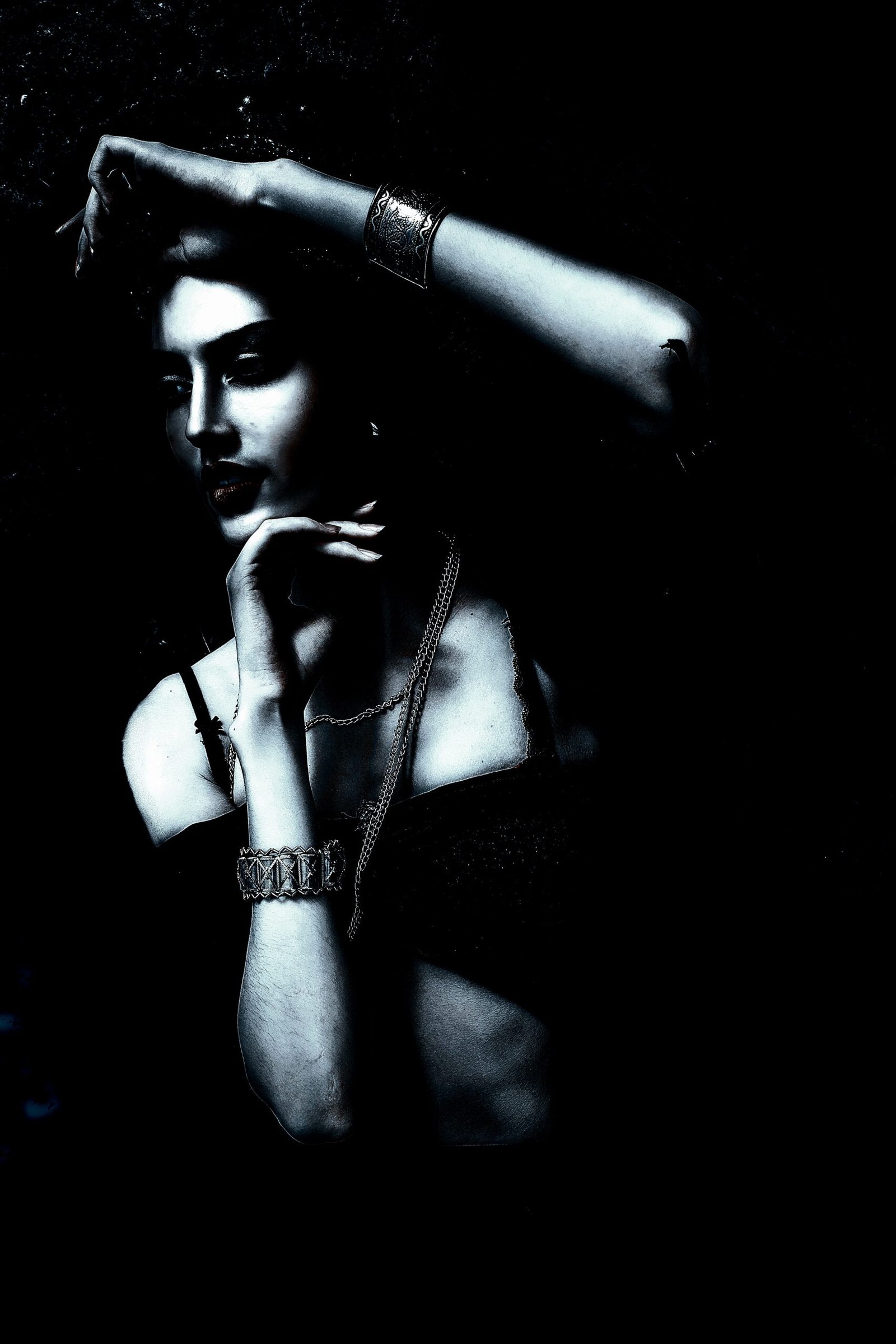 Mysterious woman wearing Gothic jewelry with moon phases and rings, surrounded by darkness.