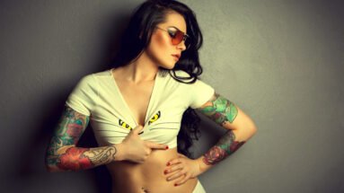 Tattooed woman in a white top with colorful arm tattoos, representing Tattoos in the Metal Subculture.