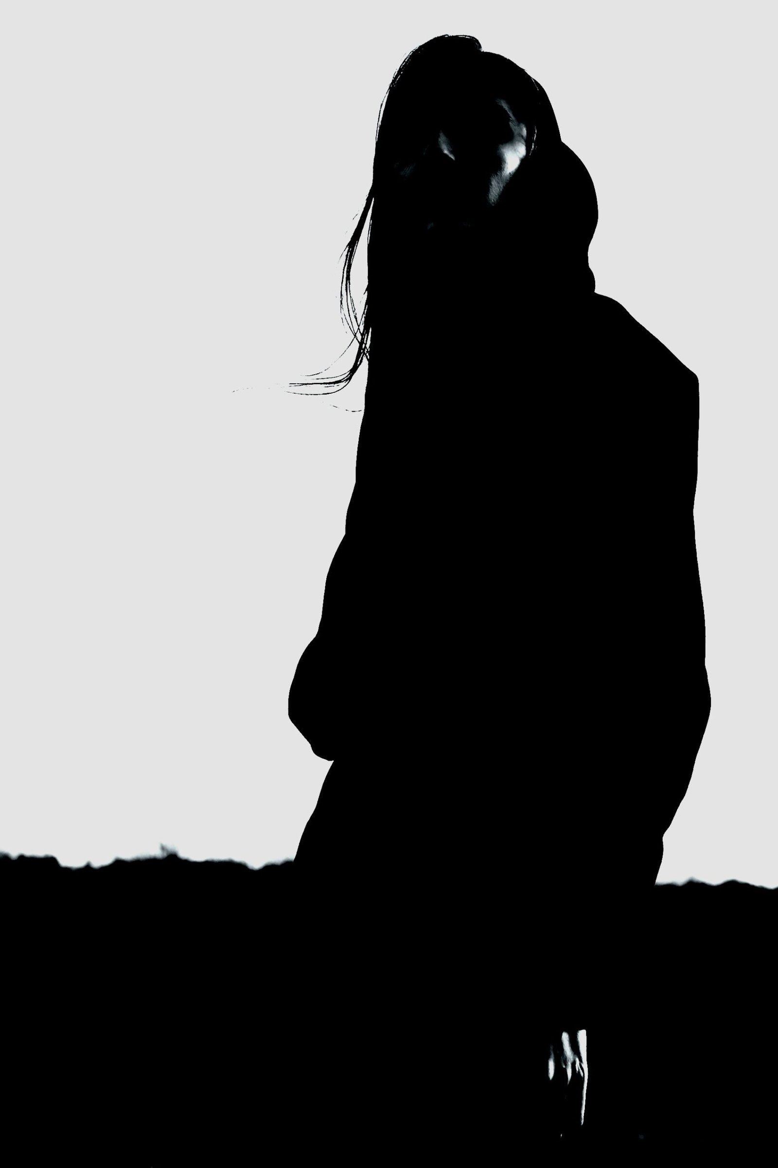 Dark and Enigmatic Goth Fashion: Silhouette of a woman wearing a hood, standing against a light background in a minimalist goth style.