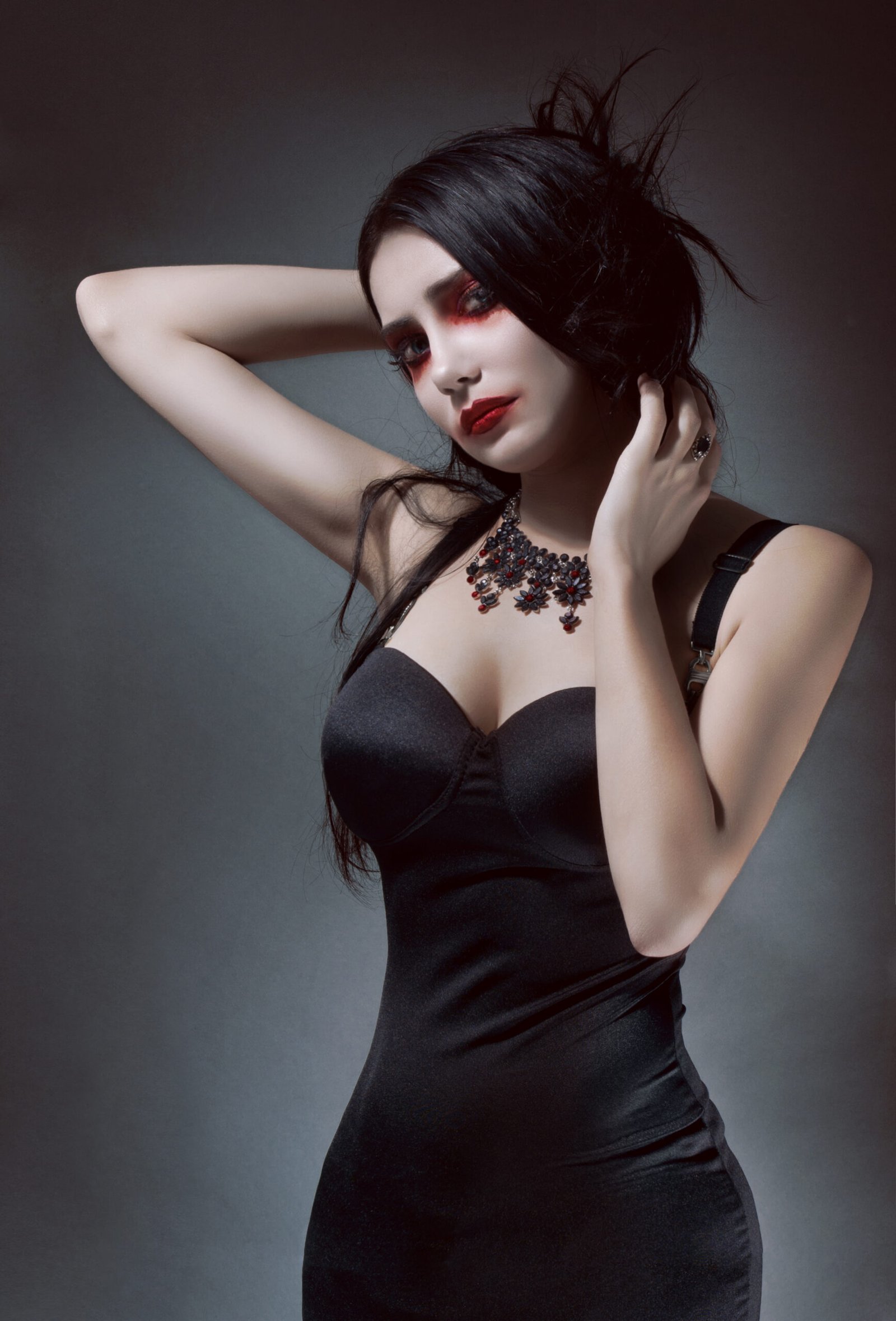 Stylish gothic woman in a black dress with a deep neckline and intricate necklace.