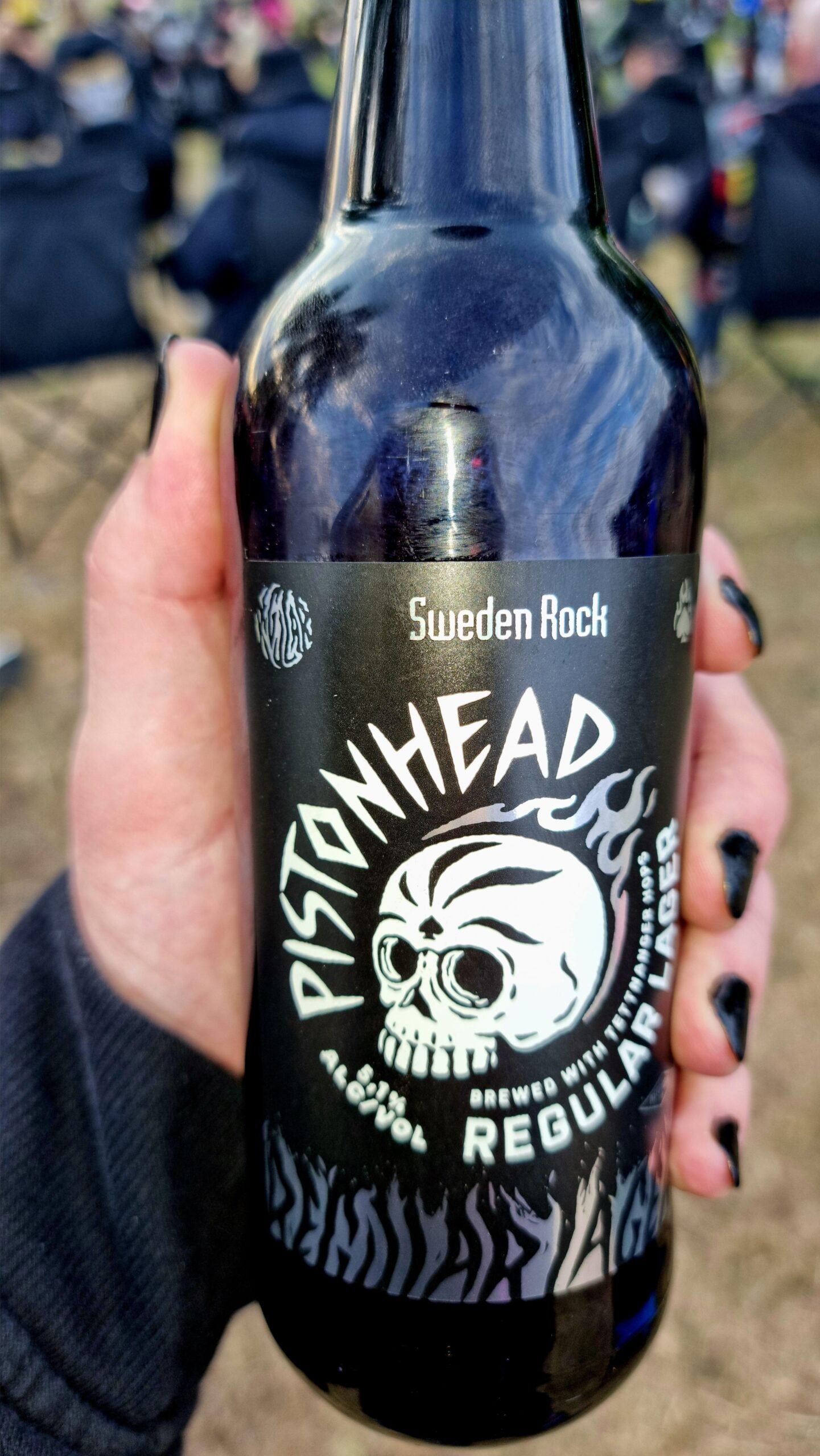 Hand holding a Pistonhead beer bottle with Sweden Rock Festival 2024 logo in the background