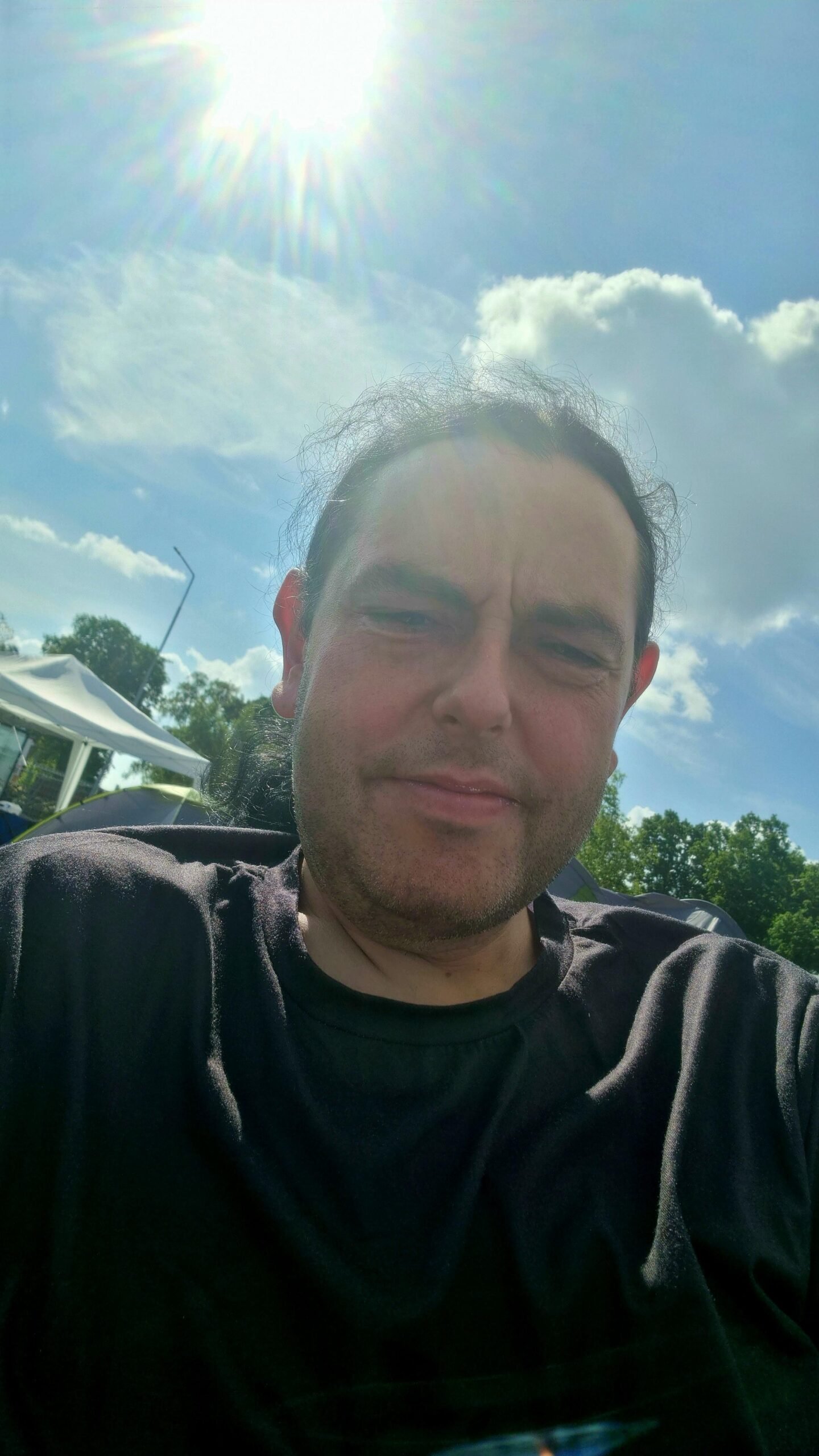 Man squinting and smiling under the bright sun at Sweden Rock Festival 2024