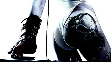 Tattooed lady in an alternative subculture DJing with a skull tattoo on her hip.