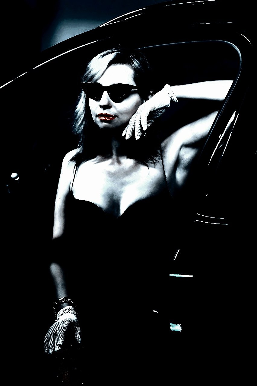 Woman with braided hair and black sunglasses looking upwards in a high-contrast, dark-themed photo.