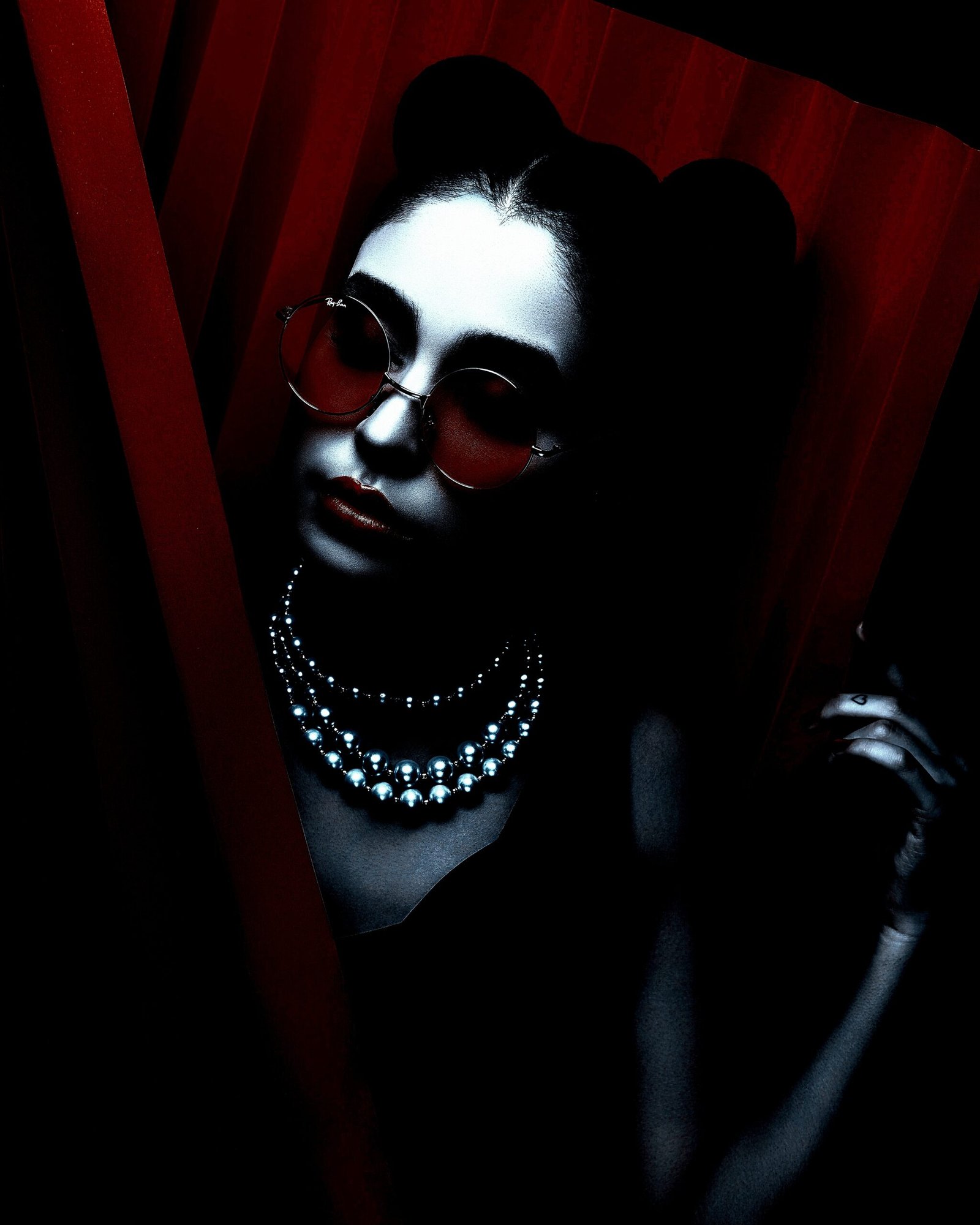 Close-up of a woman with dark hair and bold red lipstick, wearing sleek black sunglasses.