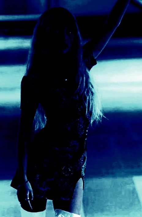 Woman in a goth summer dress with dragon motifs, standing in an empty parking garage with her arm raised.