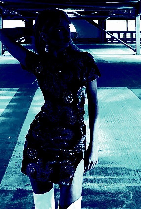 Woman wearing a short goth summer dress with dragon patterns, posing in a dark, empty parking garage.