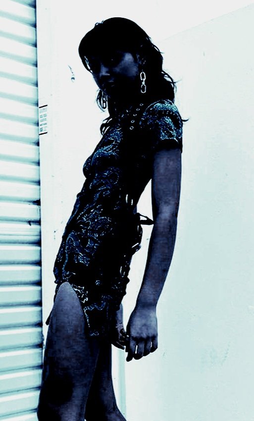 Woman in a stylish goth summer dress with dragon prints, standing against a white wall with an intense expression.