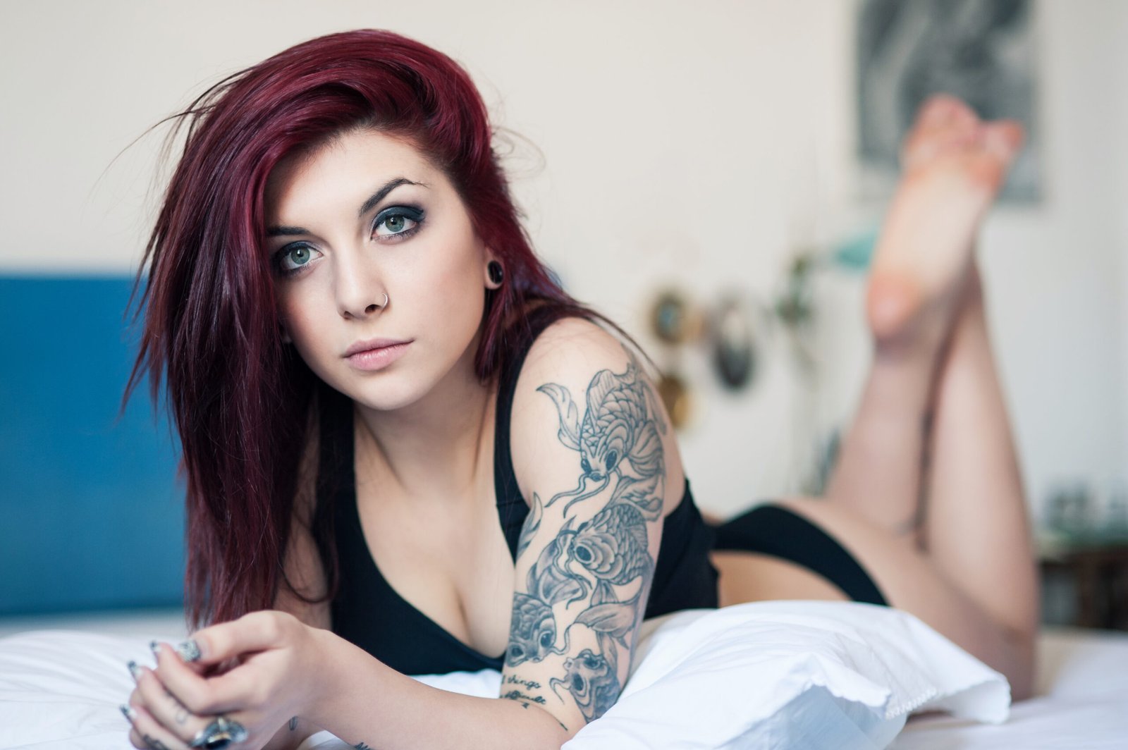 Young goth woman with red hair, lying on a bed and displaying her detailed arm tattoo.