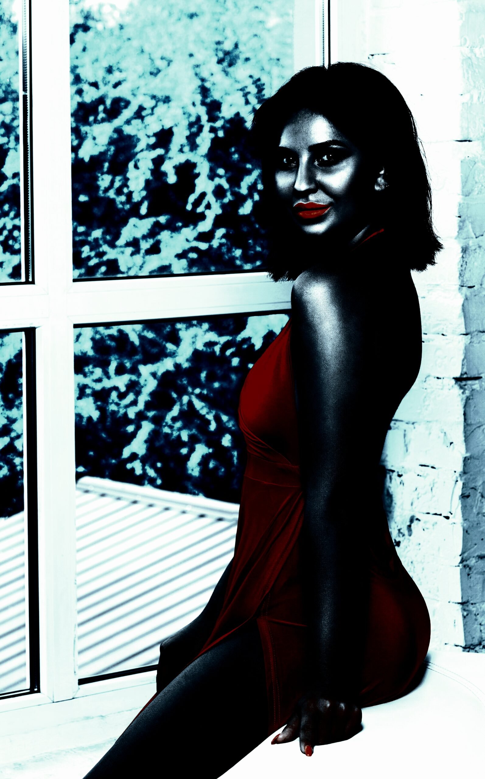 Elegant older woman in a red dress sitting by a window, exuding confidence and allure.
