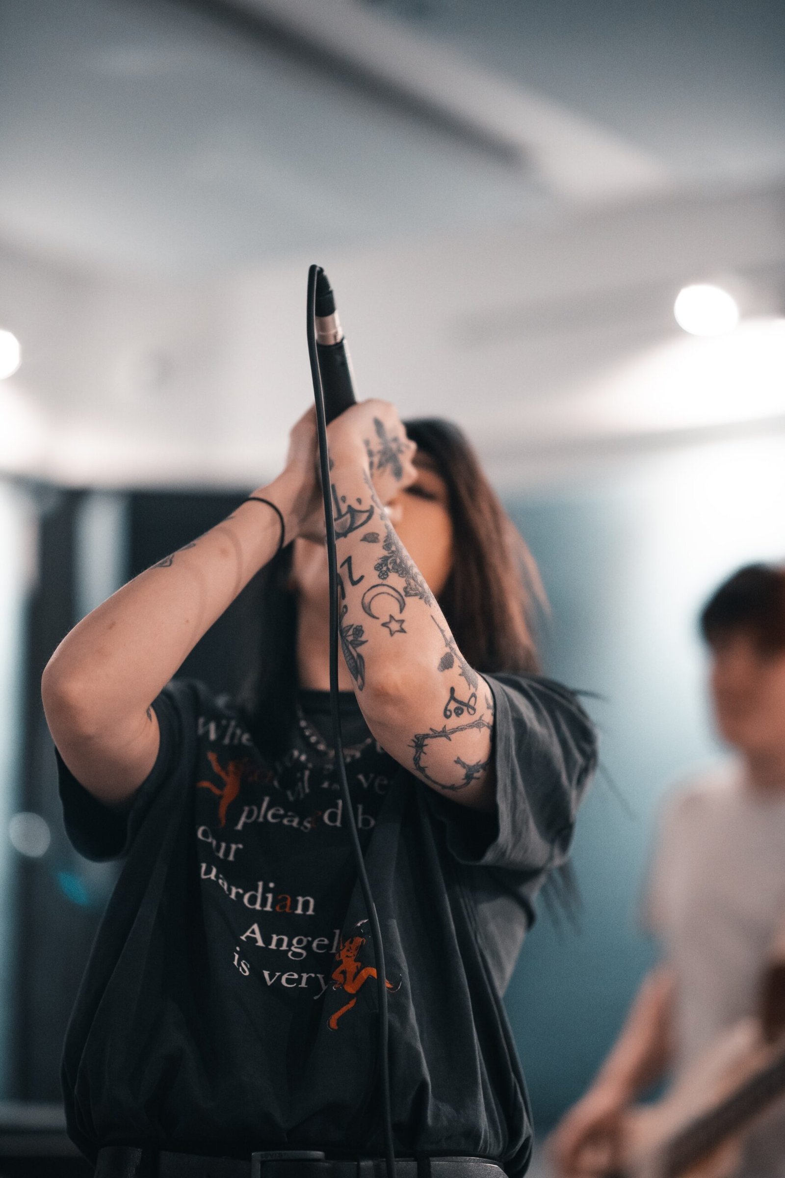 Female singer passionately performing with a microphone, showing off her heavily tattooed arms.