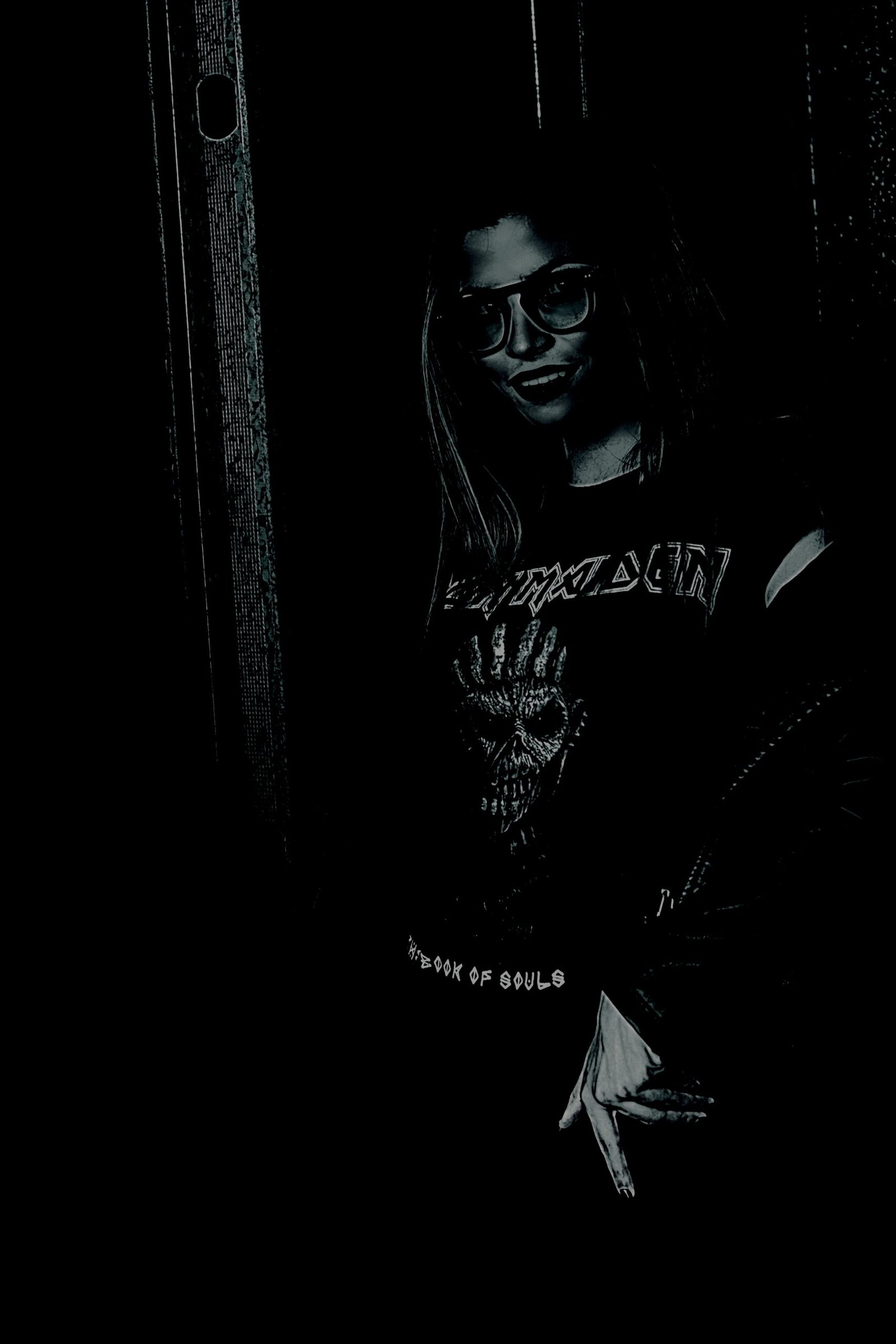Goth woman wearing an Iron Maiden T-shirt standing in a dark setting.
