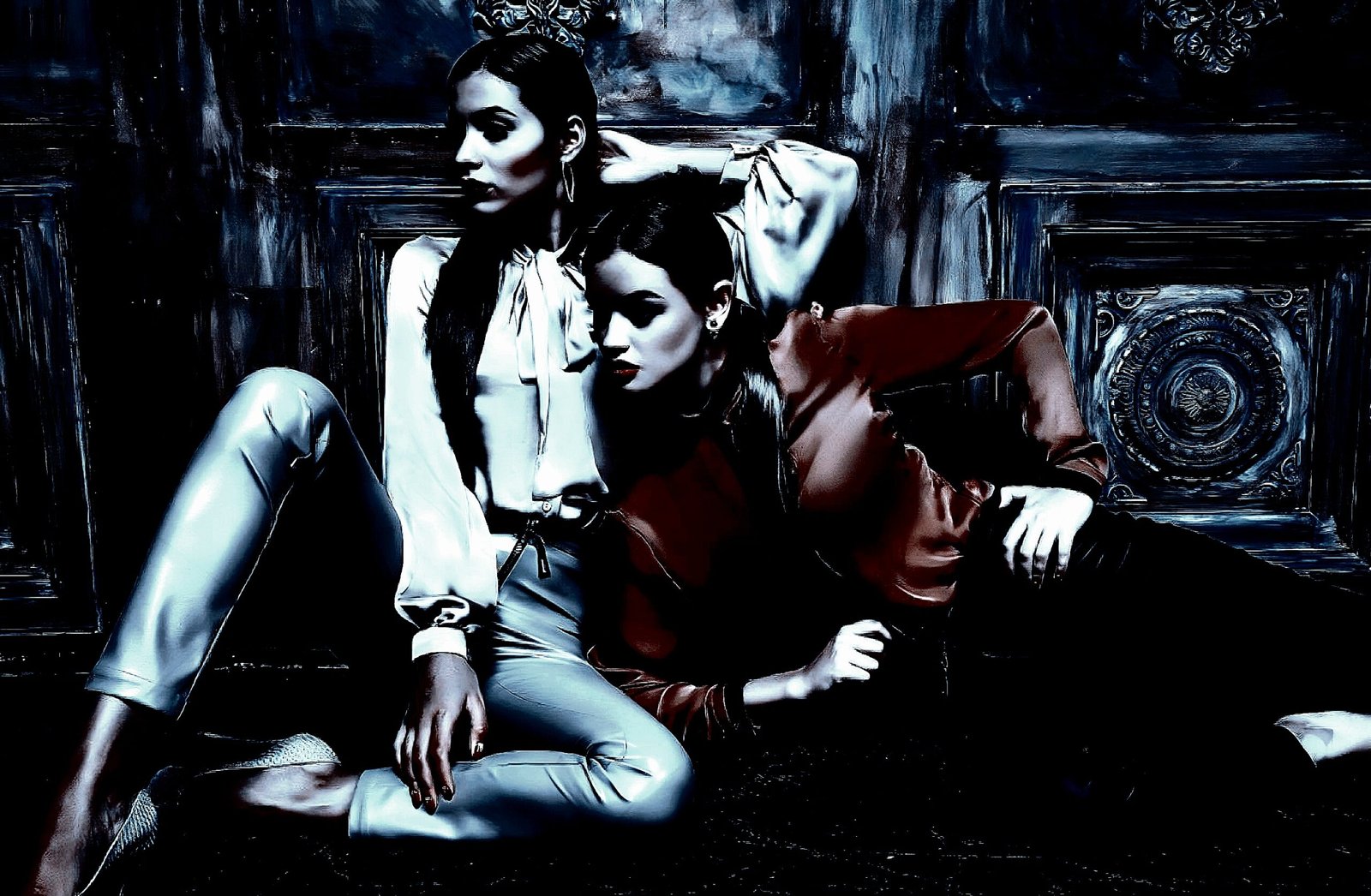 Two fashionable women posing against an ornate dark wooden background, one seated and the other leaning