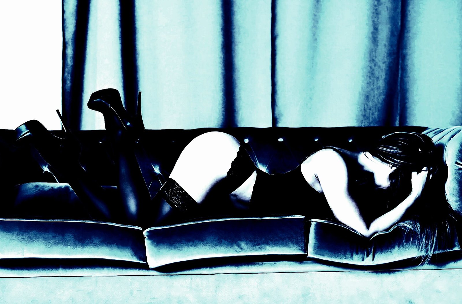 Woman in black lingerie and high heels lying face down on a blue velvet couch.
