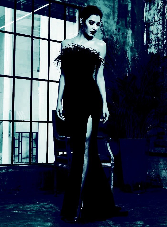 Model wearing a gothic maxi dress with feather details and a high slit, standing in an industrial setting
