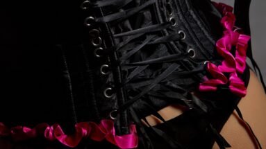 Close-up of black corset lacing with pink ribbon detailing, highlighting gothic lingerie style.